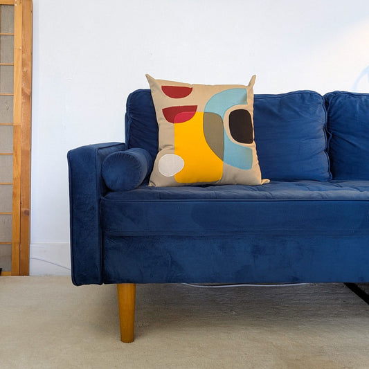 Blue sofa with a colorful pillow in a room with abstract art on the wall.
